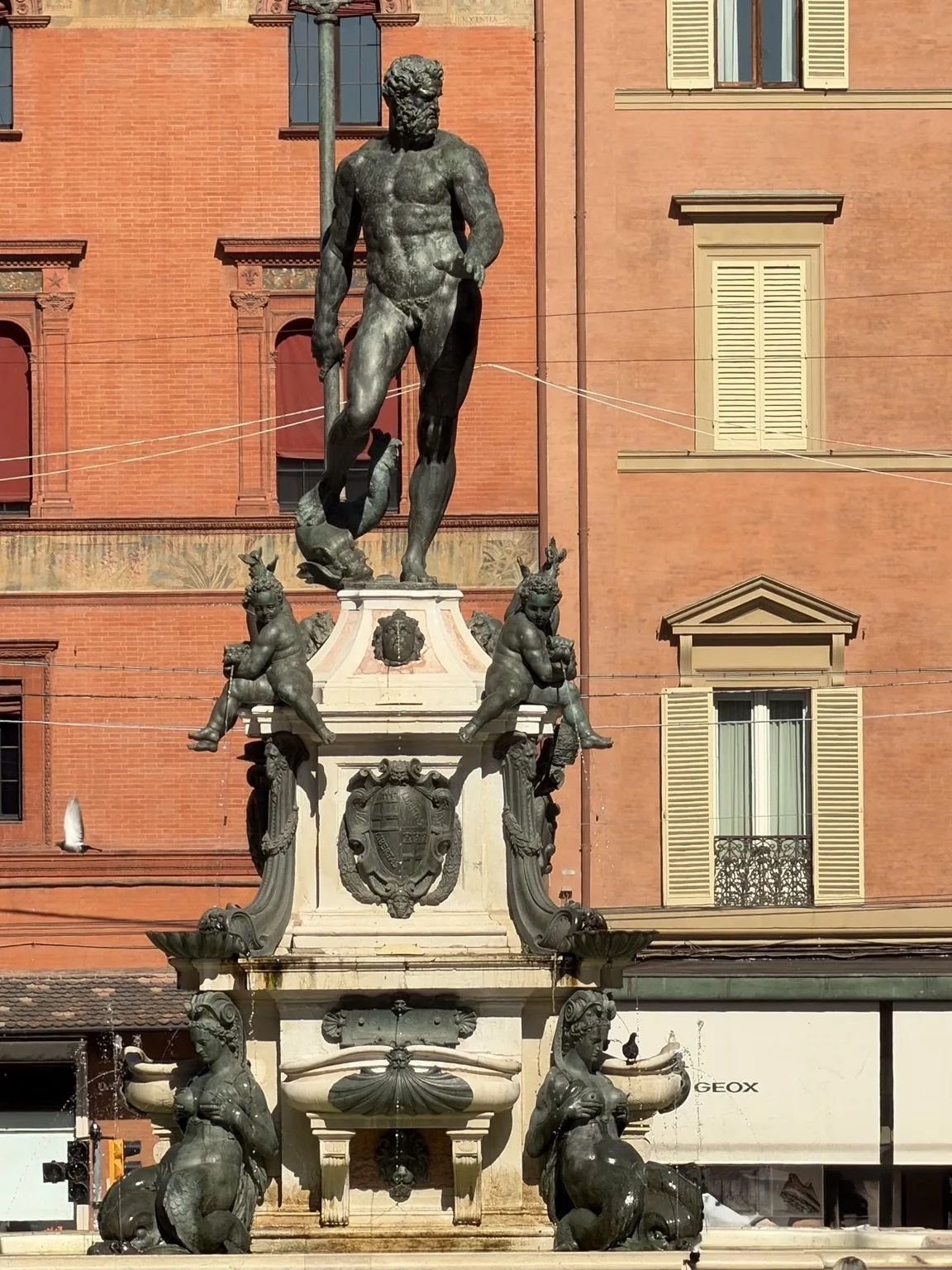 The bronze statue of Neptune on top of his fountain, with Bologna’s red buildings behind it.