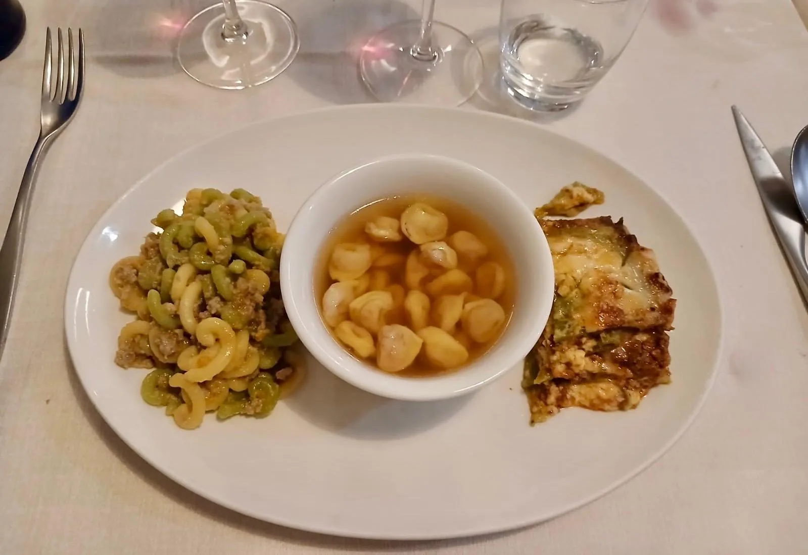 A plate with gramigna pasta and sausage, a bowl of tortellini in broth and a portion of green lasagne.