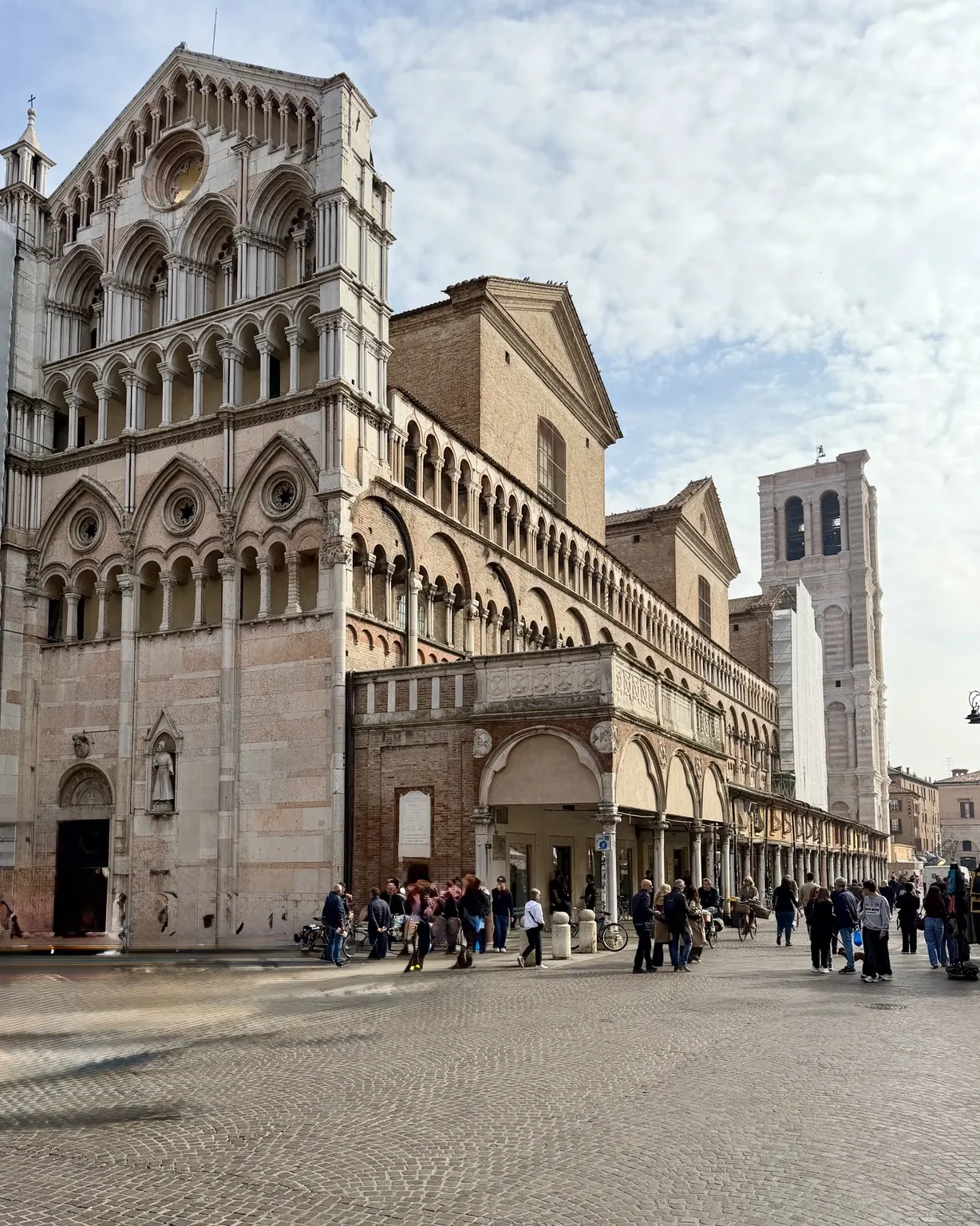 La facciata in marmo chiaro della Cattedrale di San Giorgio, con le logge ad archi e il campanile sulla destra; in piazza passeggiano molte persone.