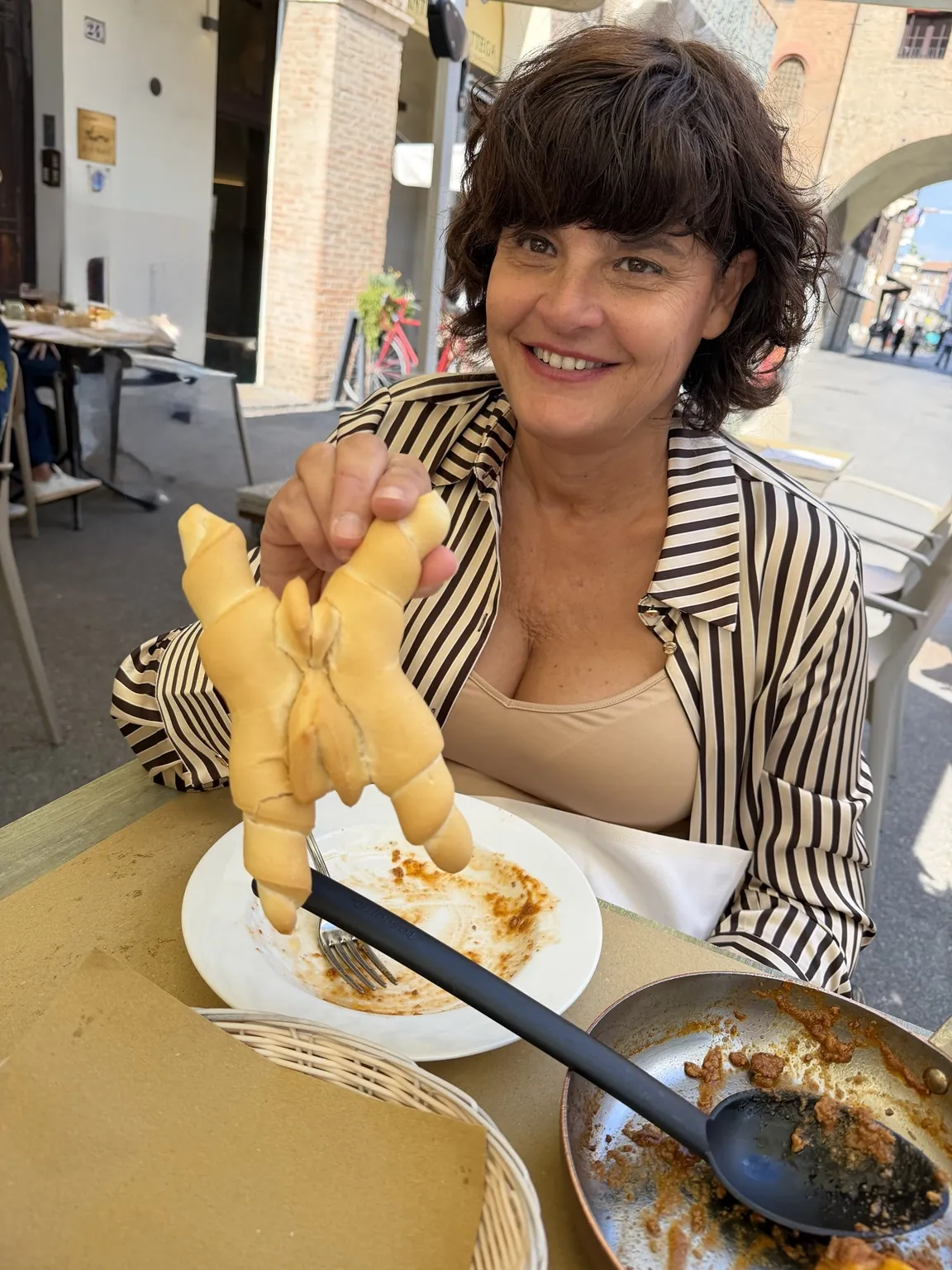 Anna sorridente a tavola mostra una Coppia Ferrarese, il pane a forma di croce con le punte ritorte.