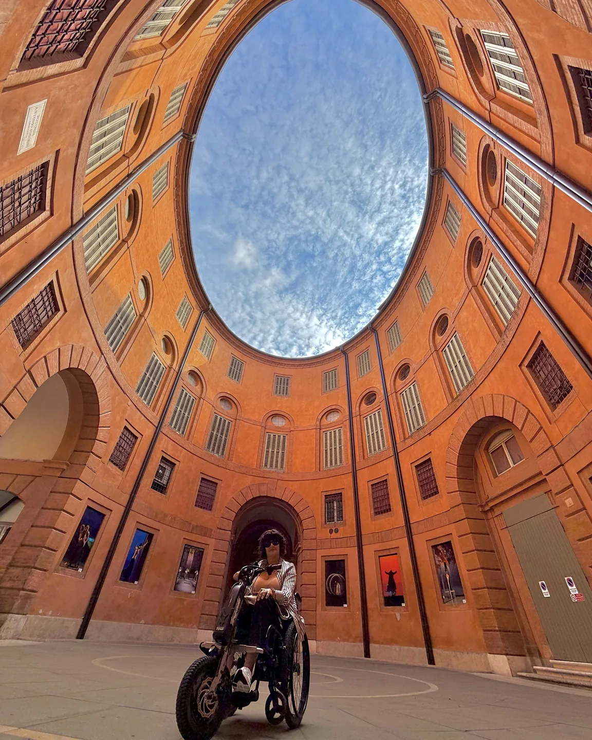 Anna sul suo Triride al centro della Rotonda Foschini: le pareti color arancio con le finestre salgono verso un’apertura ovale sul cielo azzurro.