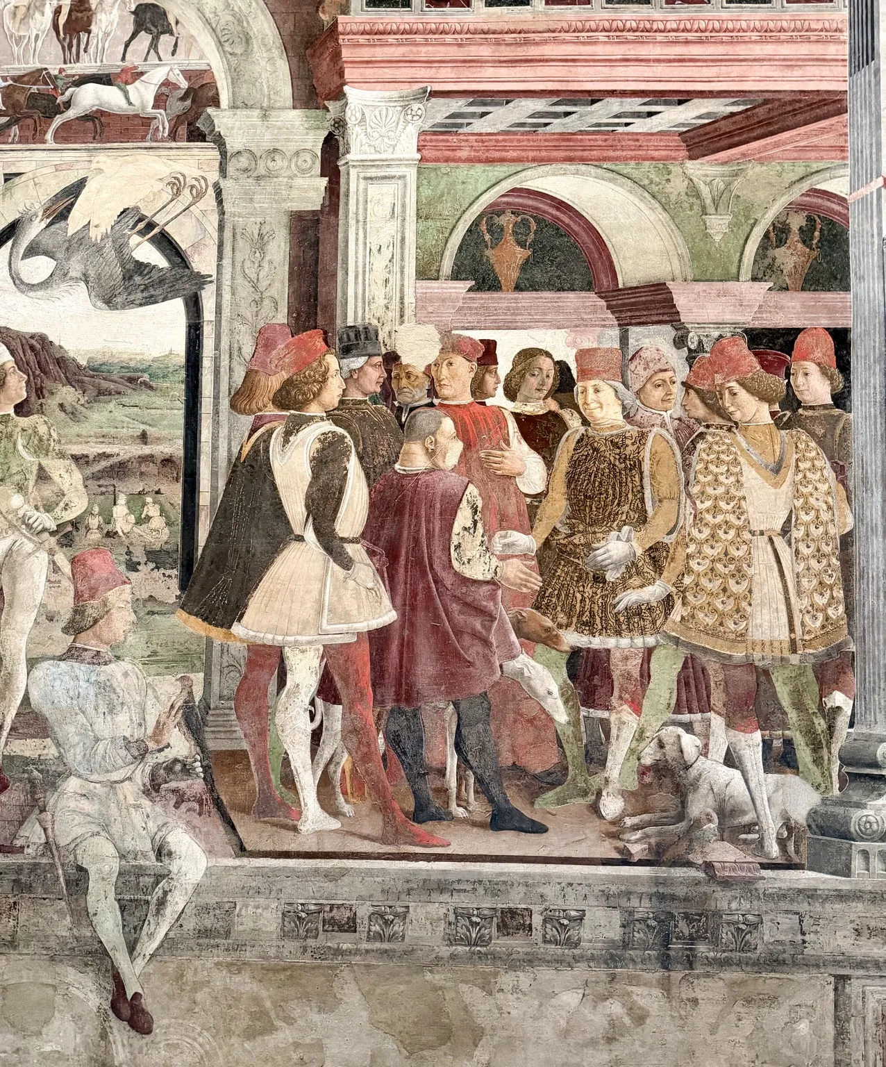 Particolare dell’affresco del mese di Aprile: un gruppo di cortigiani in abiti rinascimentali dai colori vivaci, tra cui Borso d’Este nell’abito dorato, con un cane ai loro piedi.
