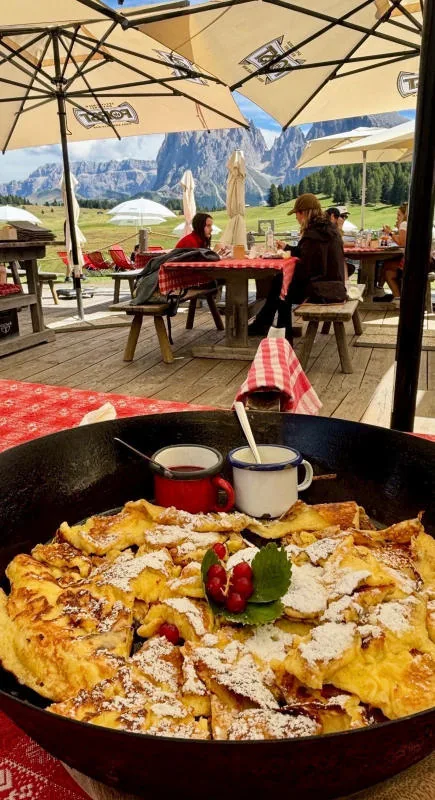 A pan of Kaiserschmarrn on the chalet table, with the terrace and the mountains in the background.