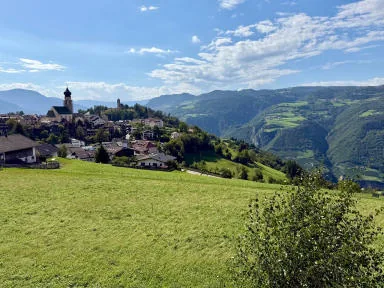 The village of Fiè with its bell tower, among green meadows and wooded mountains.