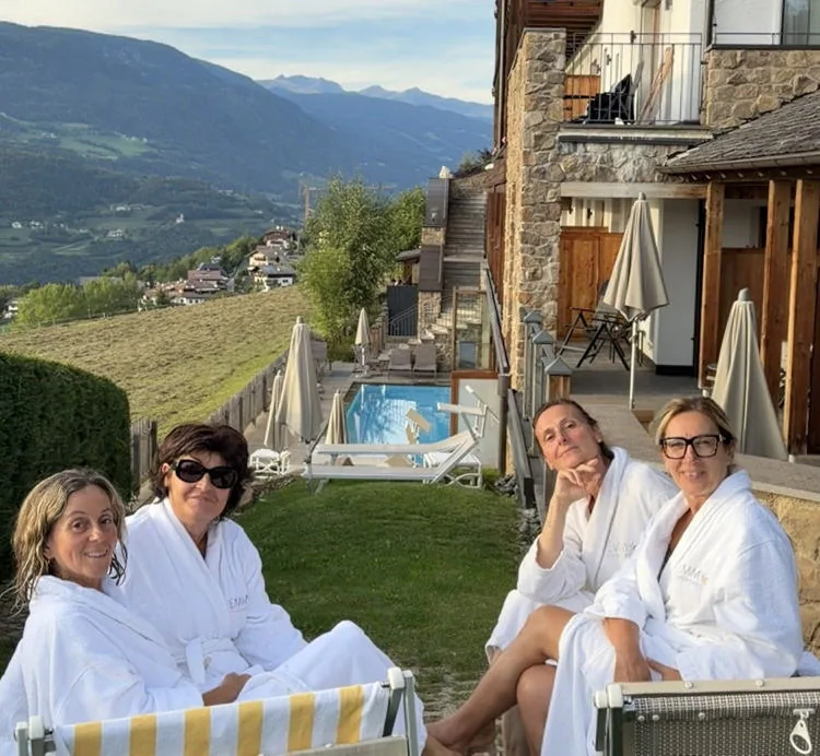 Anna and three friends in white bathrobes sitting on the lawn by the pool.