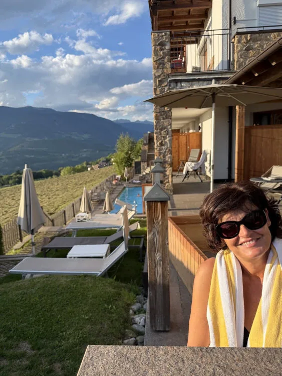 Anna in a bathrobe on the terrace of the room; behind her the lawn with sun loungers and the pool.
