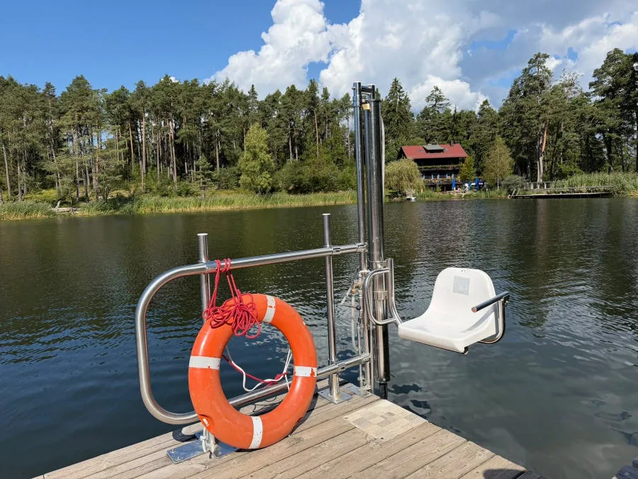 On the lake’s wooden jetty, the lift with a white seat for getting into the water, next to an orange lifebuoy.
