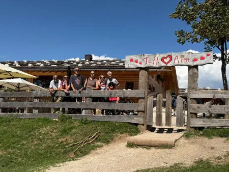 The group of friends behind the fence at Malga Tuff, under the wooden sign with a heart.