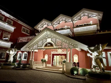 The pink façade of a Tyrolean-style building lit up at night, with white wooden decorations.