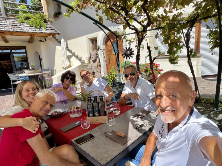 A group selfie at the table under a pergola: five smiling friends.