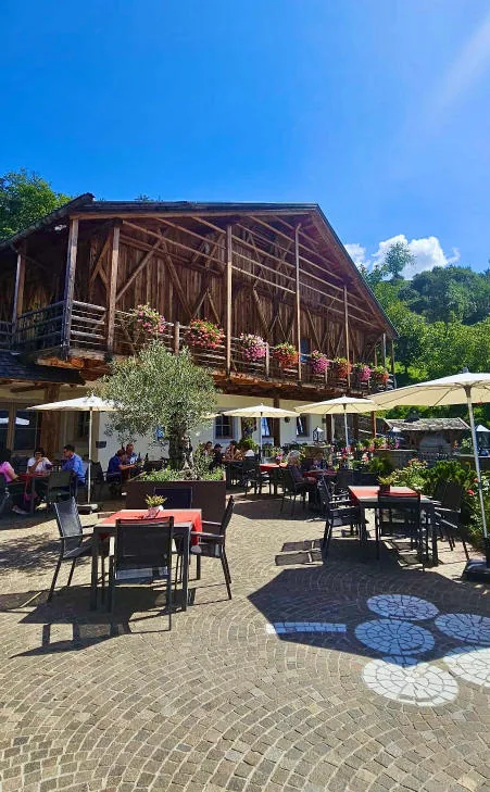 The terrace of the Pitschlmann farmhouse with tables and parasols, beneath a large wooden barn.