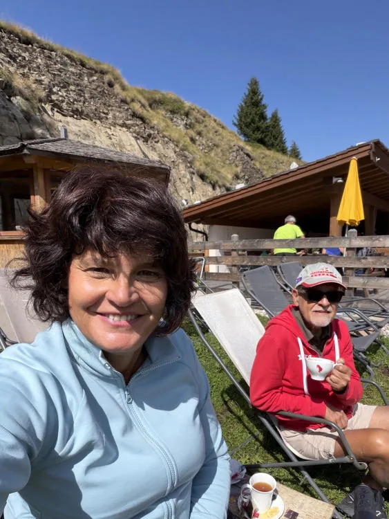 Anna smiling in the foreground; behind her, her companion on a deckchair and the terrace of the hut.
