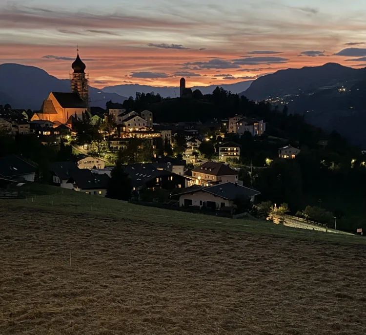 The village of Fiè lit up at dusk, with its bell tower and a pink and orange sky.