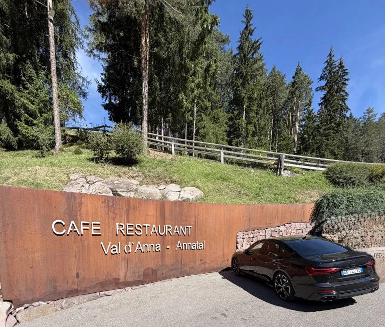 A car parked next to the «Café Restaurant Val d’Anna» sign, at the edge of the woods.