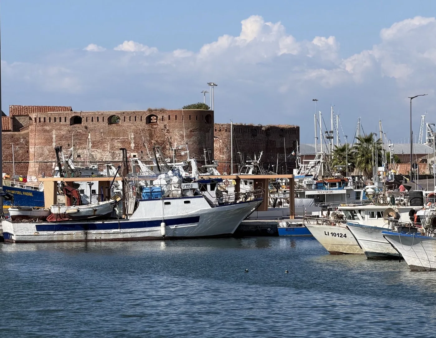 The brick Fortezza Vecchia overlooking the water, with fishing boats and other boats moored in the harbour.
