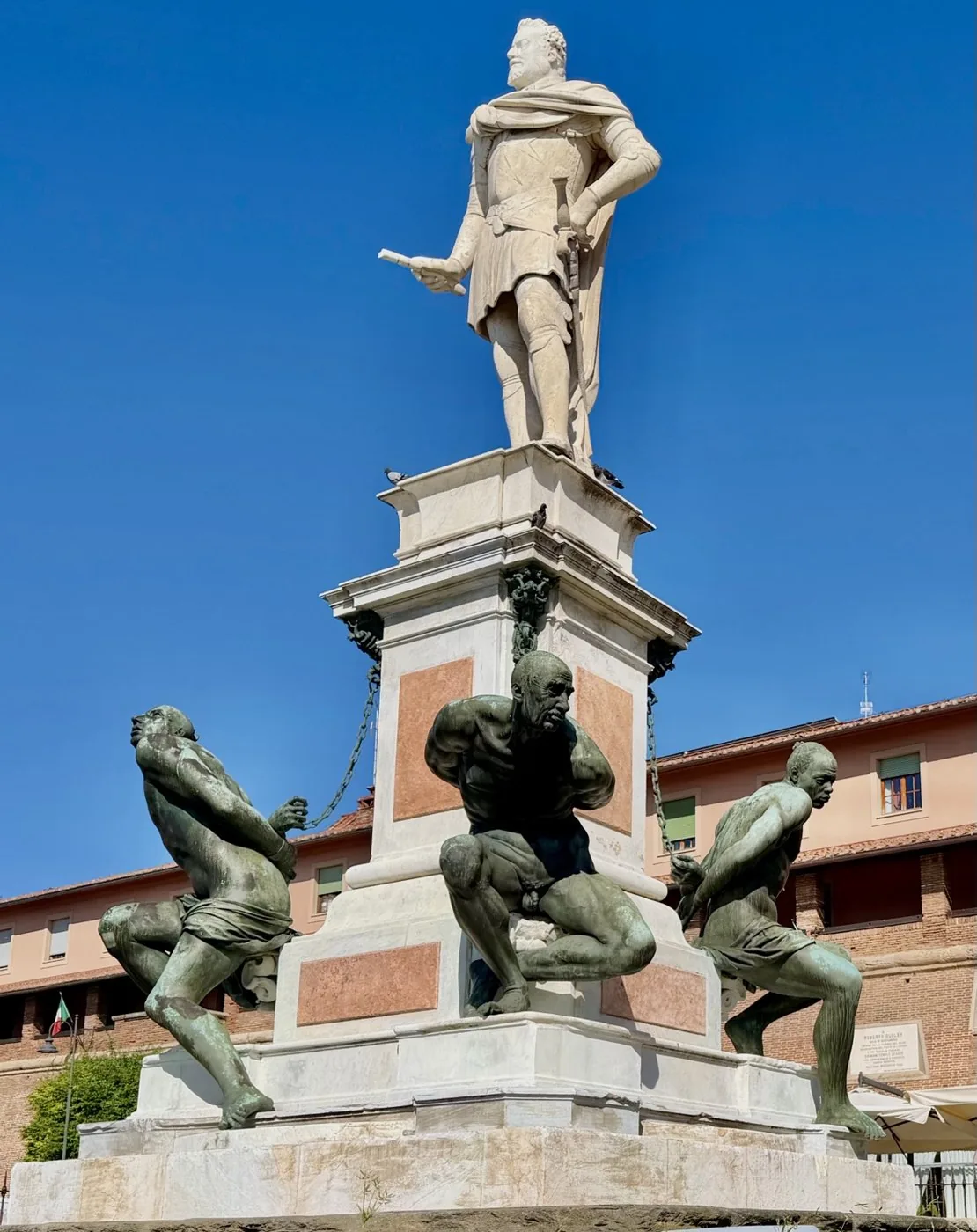 The Monument of the Four Moors: the marble statue on top and the chained bronze figures at the base, under a blue sky.