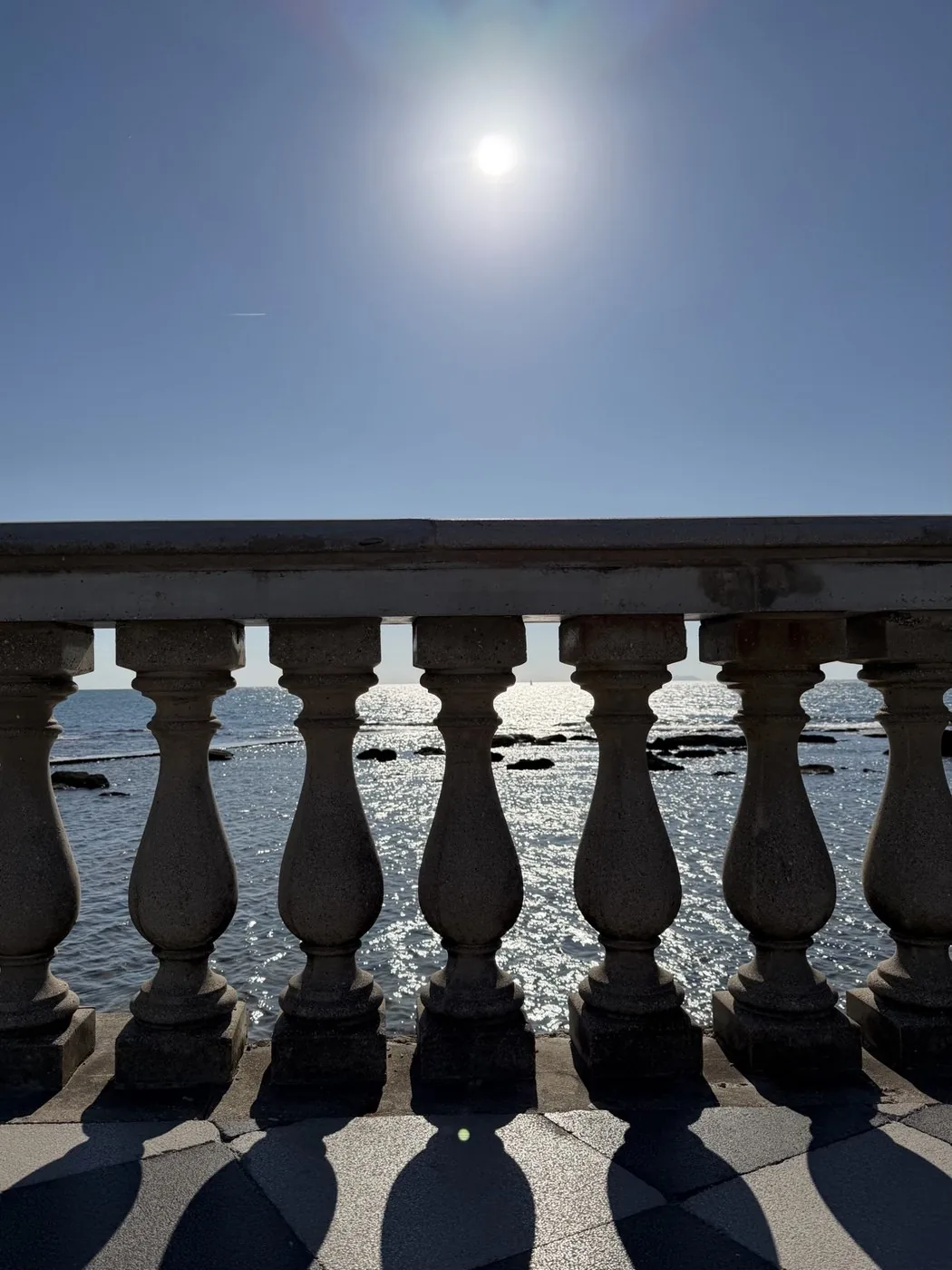 The balustrade of Terrazza Mascagni against the light, with the sun high over the shimmering sea.