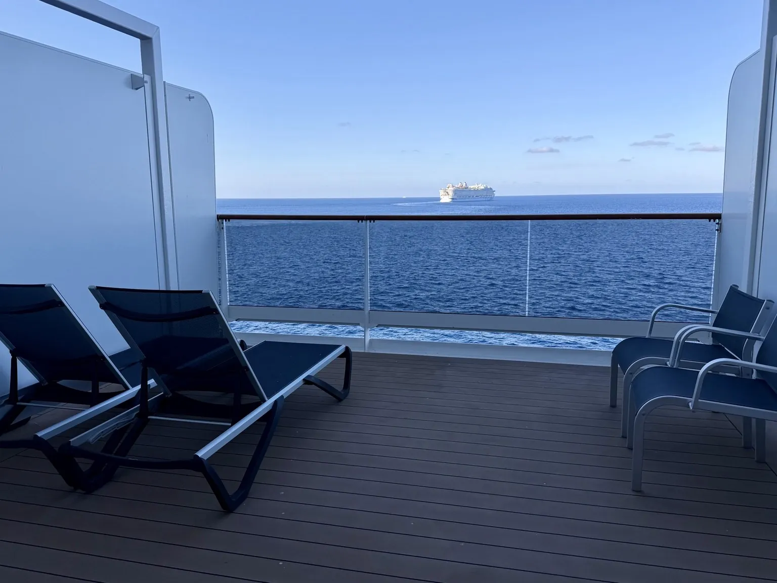 A wide balcony with two sun loungers and two armchairs, looking out over the open sea.