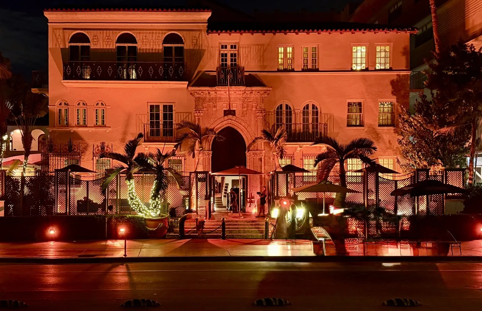 The façade of Casa Casuarina bathed in warm red light, at night.