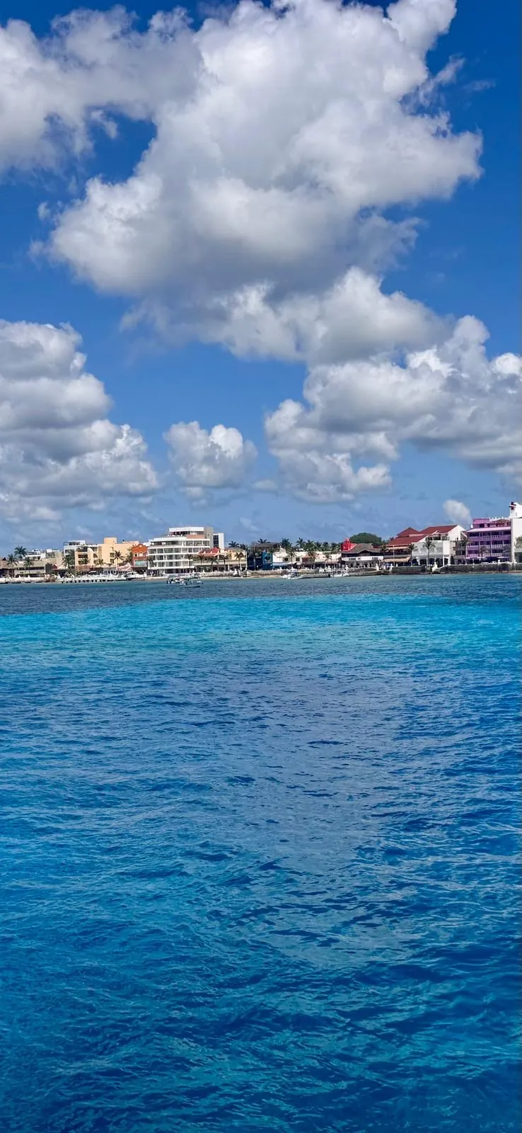 The sea shading from turquoise to deep blue, with the town on the horizon and big white clouds.