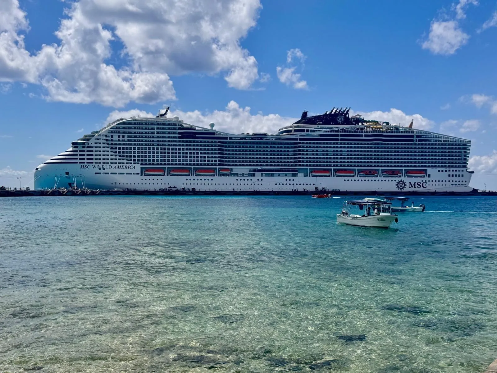 The big white cruise ship moored offshore, beyond the shallow, clear water.