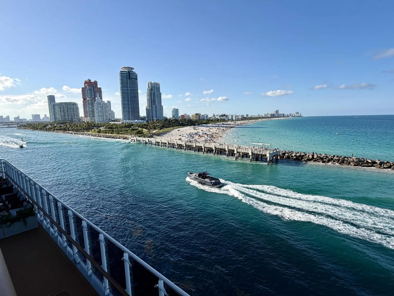 The skyscrapers and beach of Miami Beach seen from high up on the ship, with a speedboat leaving a white wake.
