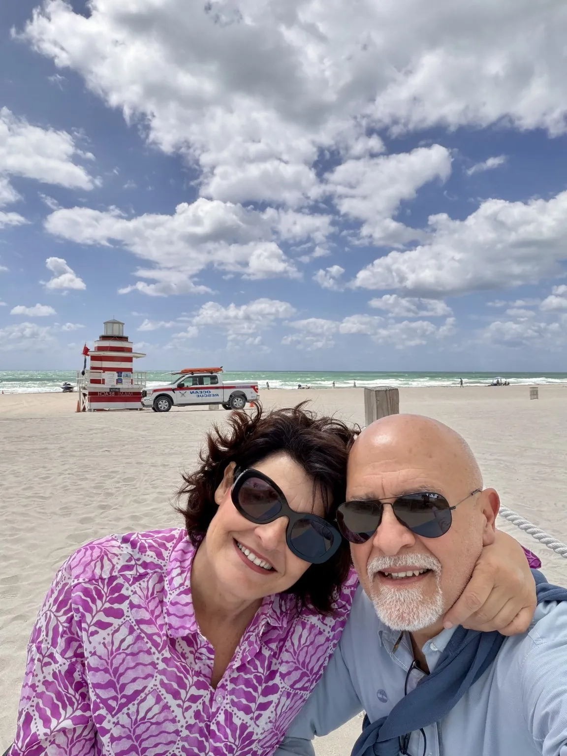 Anna and her companion smiling in a selfie on the beach, under a sky full of clouds.
