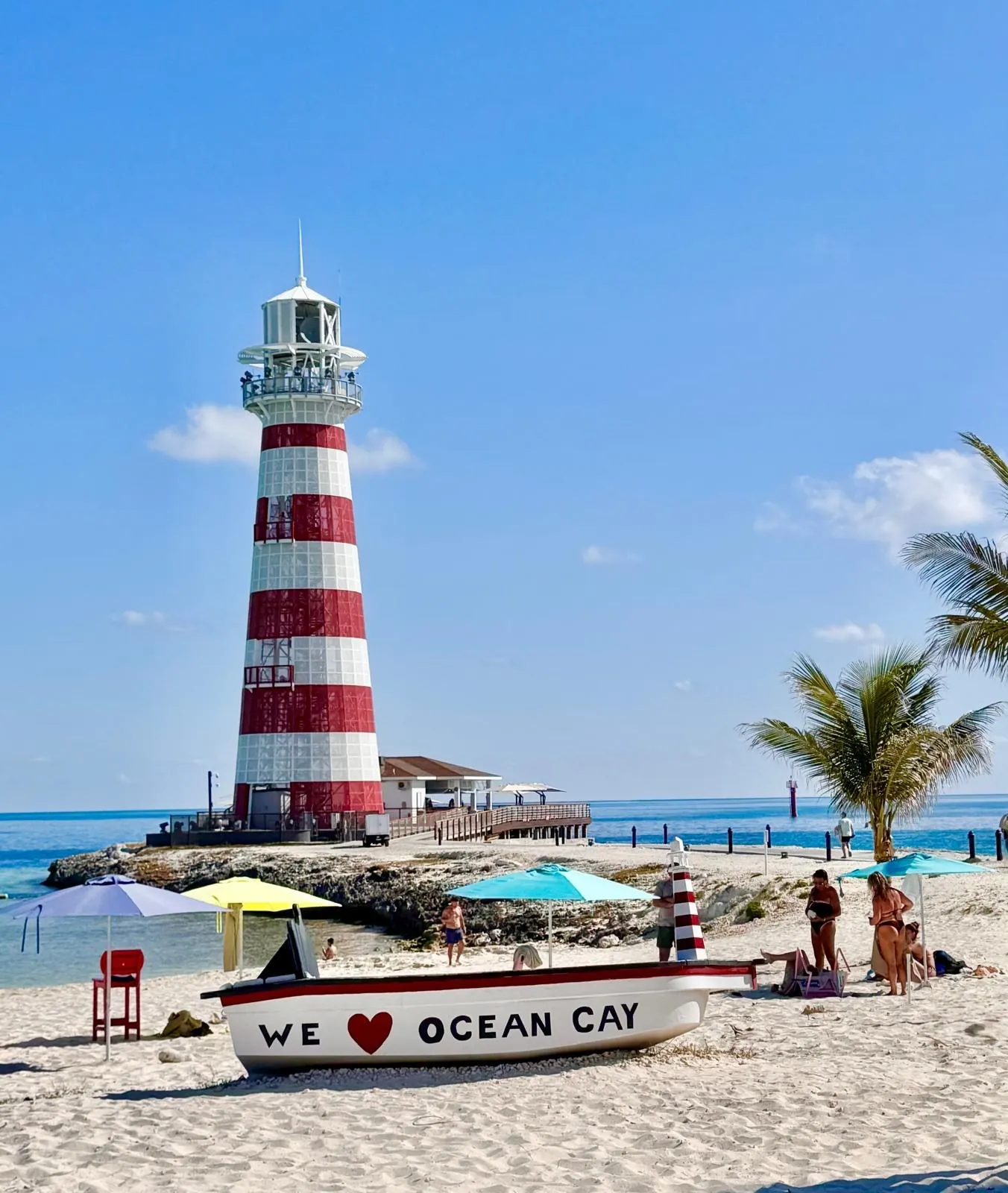 A red-and-white striped lighthouse on the beach; in the foreground, a little boat with the words “We love Ocean Cay”.
