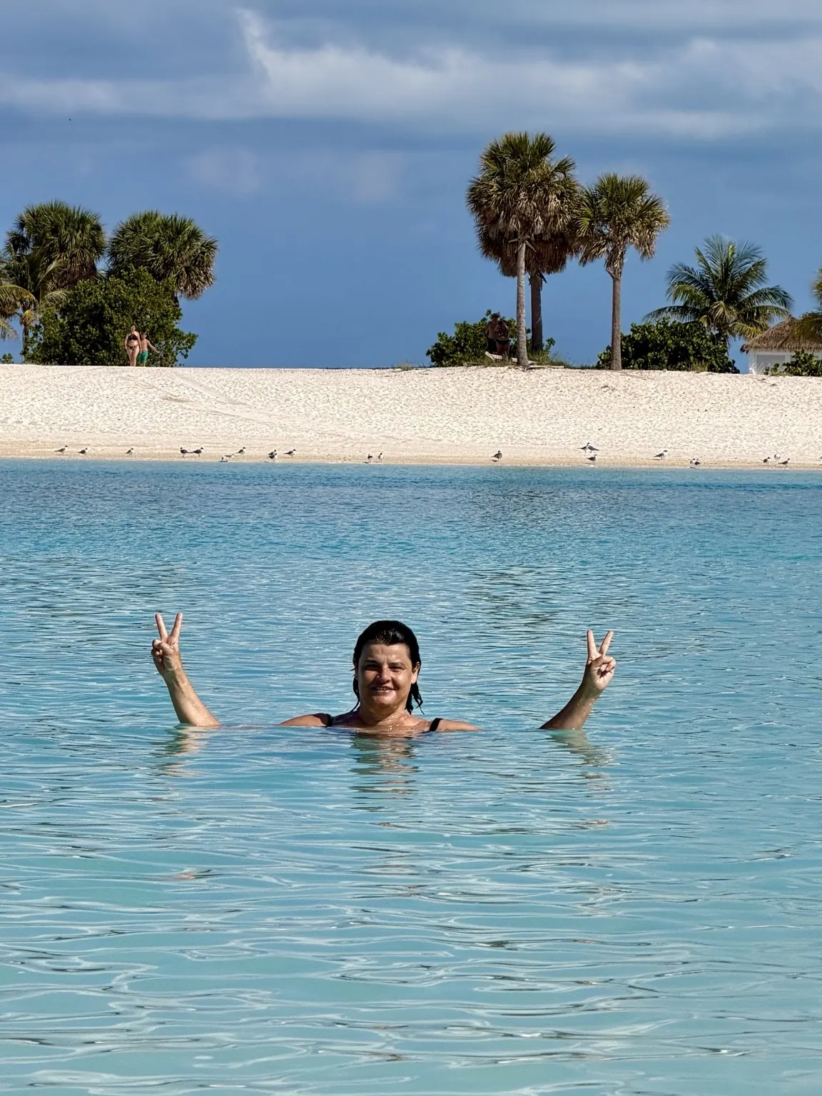 Anna in the water, smiling and raising her arms with a victory sign on both hands.