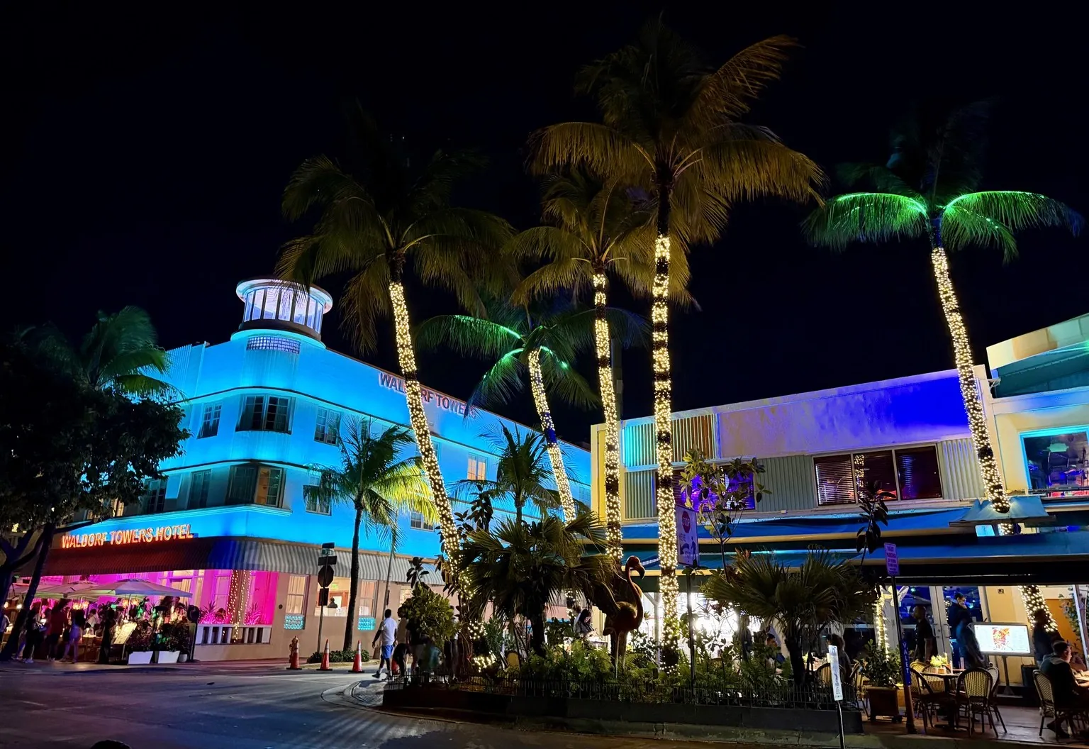 Art Deco hotels lit by blue and pink neon, with the palm trees wrapped in lights.