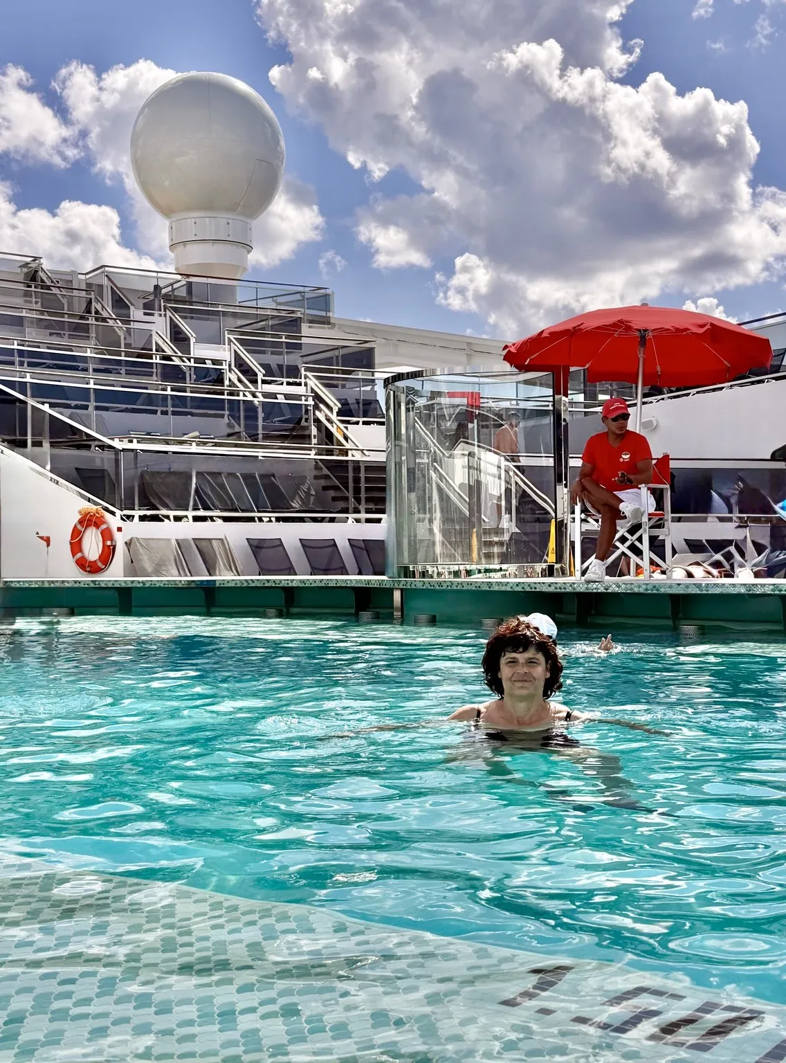 Anna in the turquoise water of the pool, under a sky with big clouds.