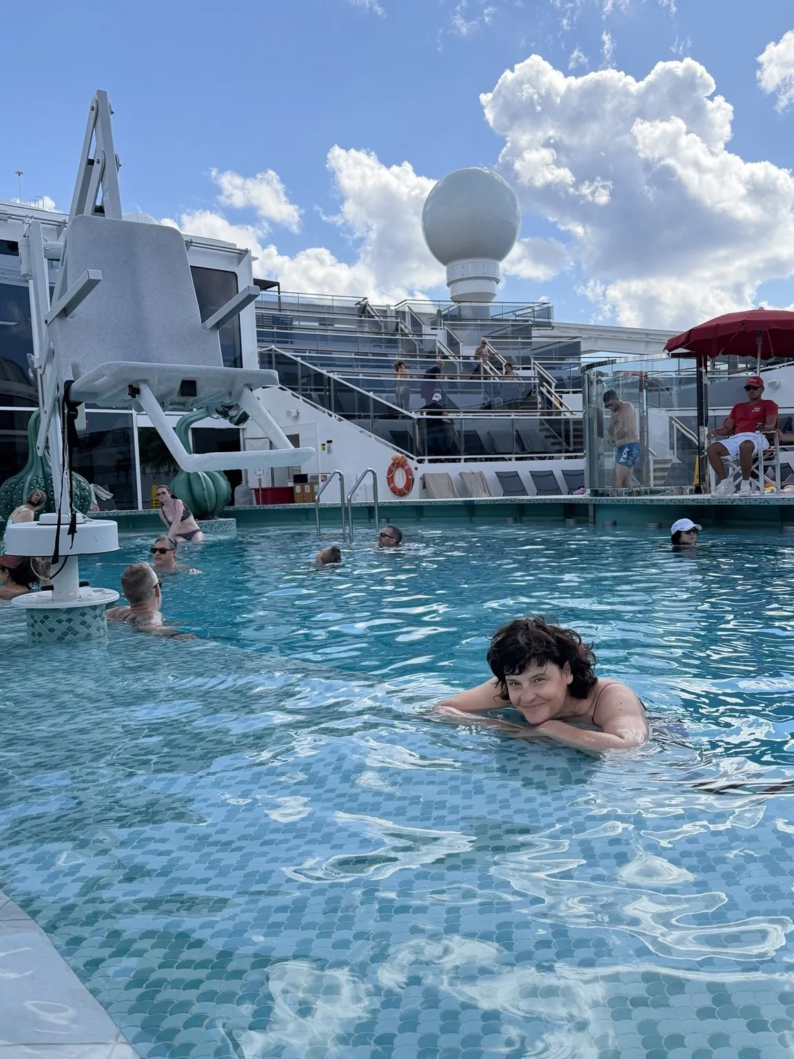 Anna in the water of the pool, leaning on the edge, with the ship’s deck behind her.