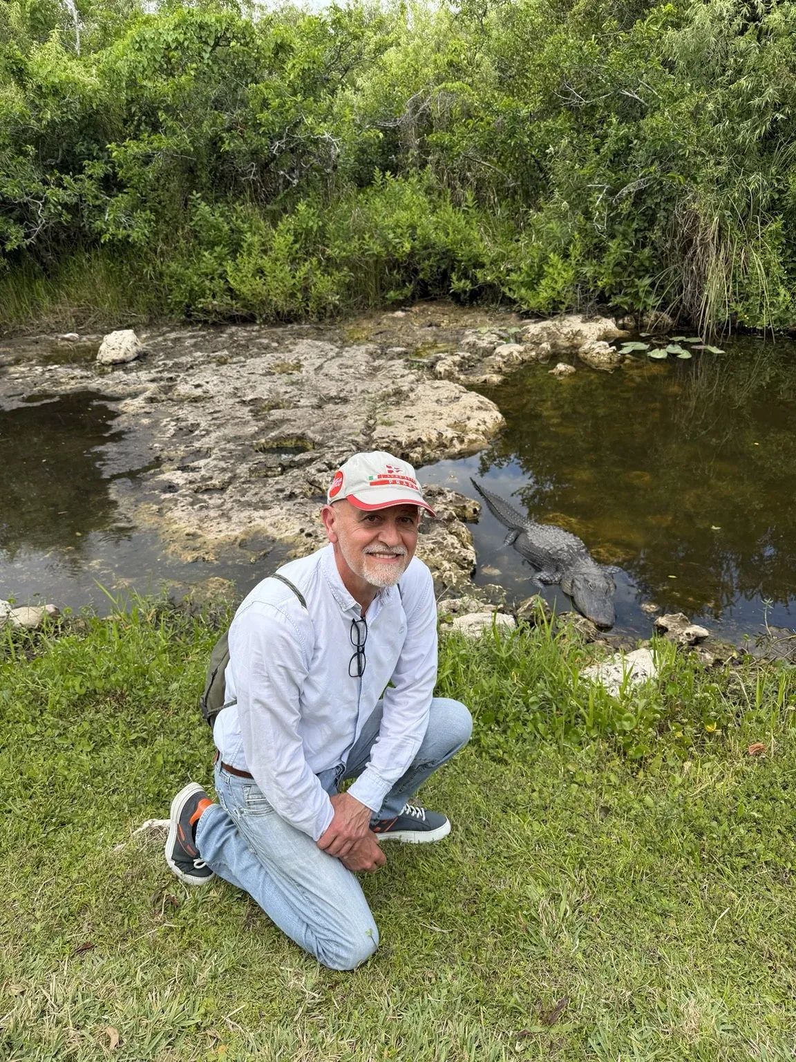 Anna’s companion crouching on the grass; behind him, near the water, an alligator can just be seen.