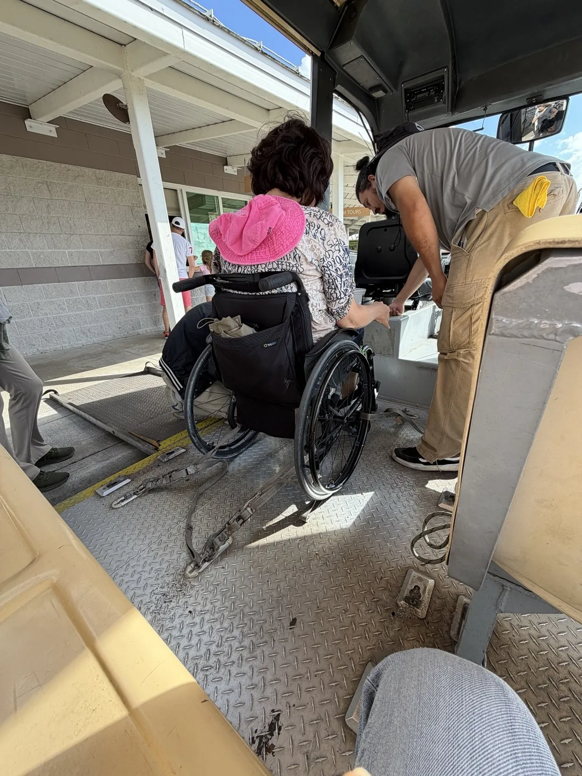 A member of staff helps Anna board the tram in her wheelchair, up a metal ramp.