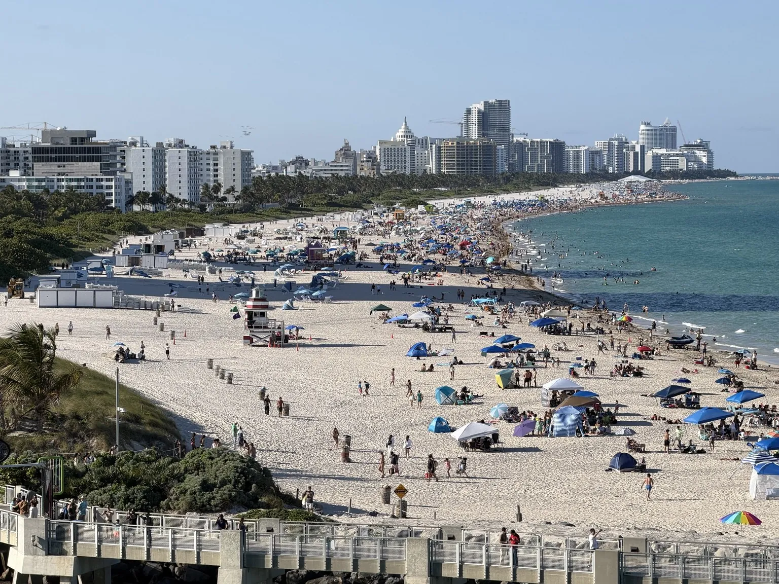 The long beach of South Beach crowded with parasols, seen from above, with the buildings behind it.