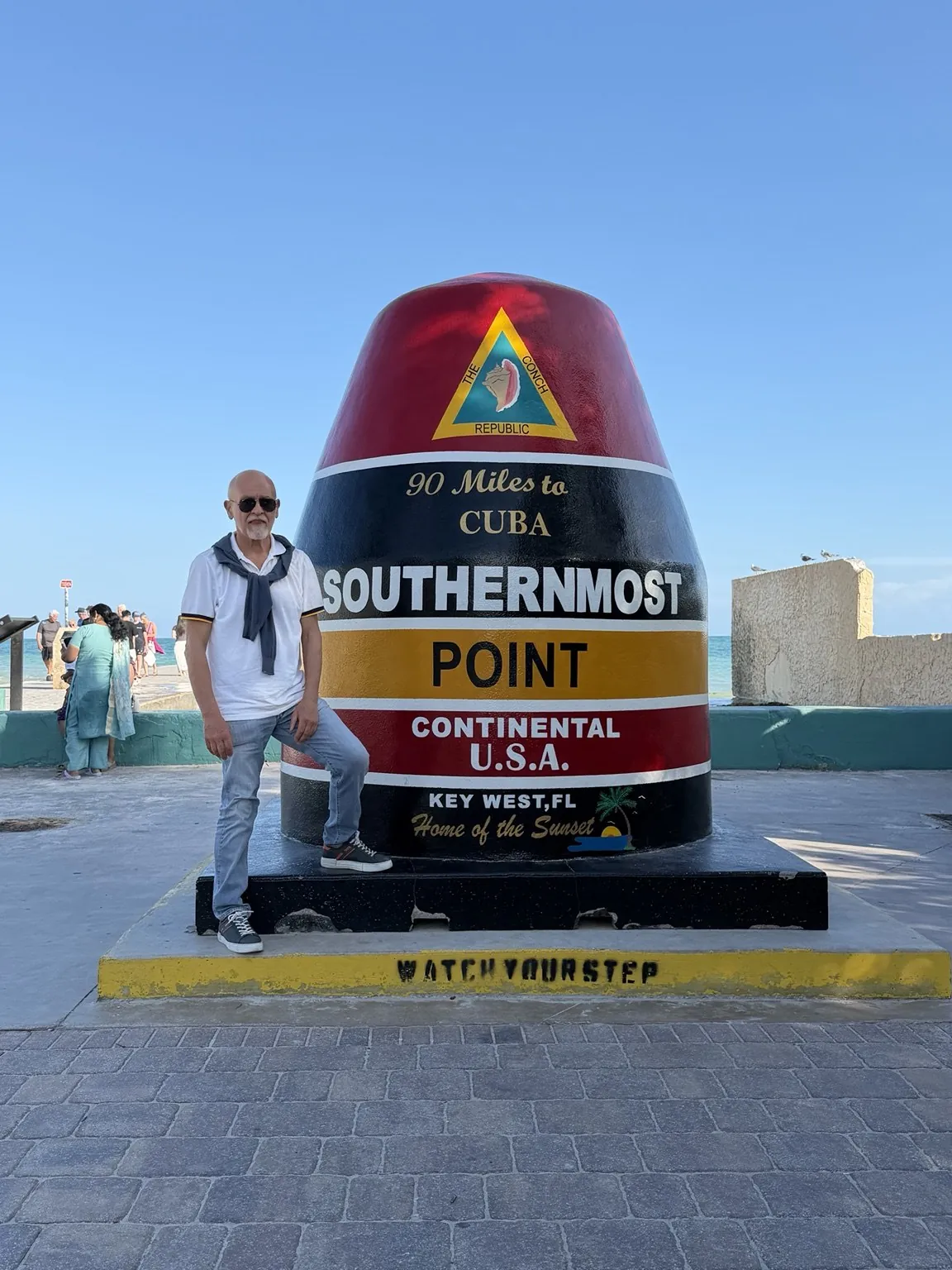 Anna’s companion standing beside the buoy-shaped marker with the words “90 Miles to Cuba”.