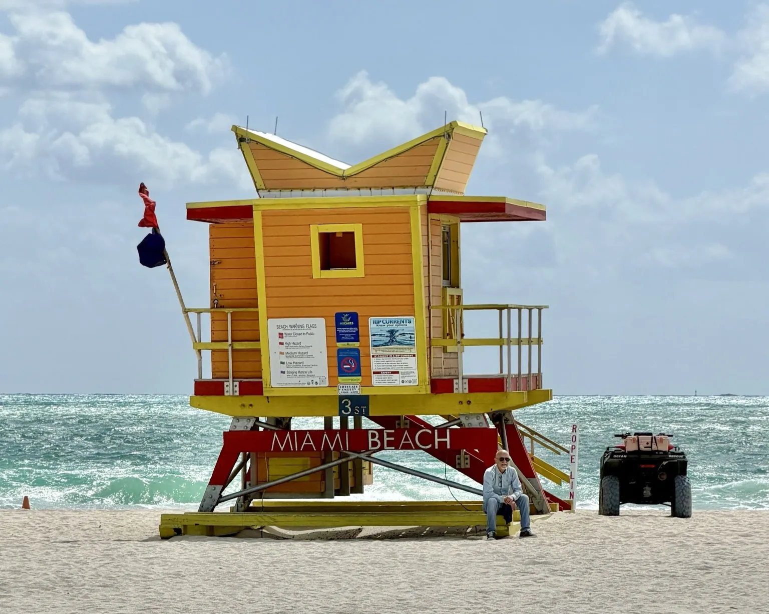 An orange and yellow lifeguard tower with the words “Miami Beach”, in front of a choppy ocean.