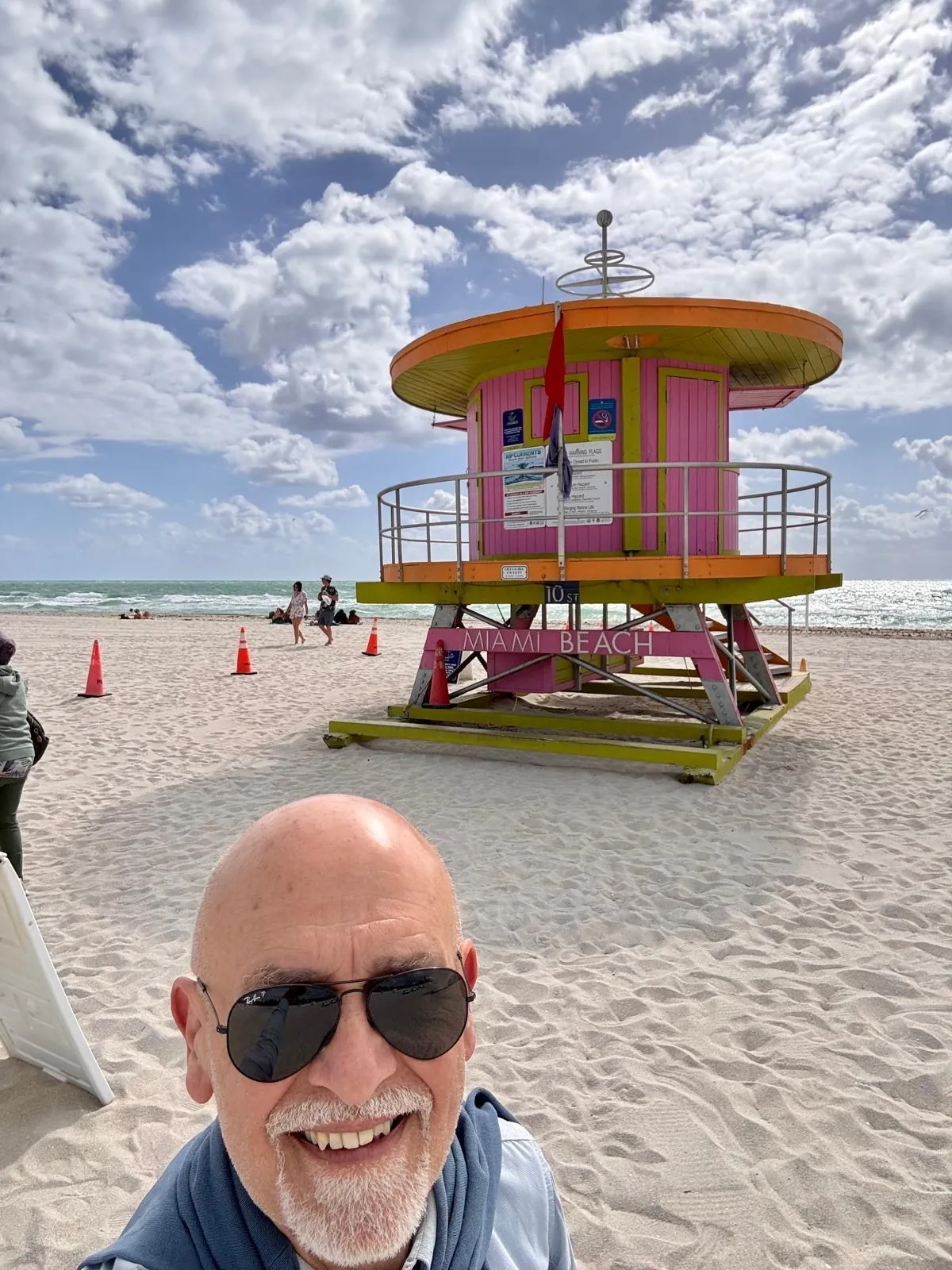 Anna’s companion in the foreground on the beach; behind him, a pink, yellow and green lifeguard tower.