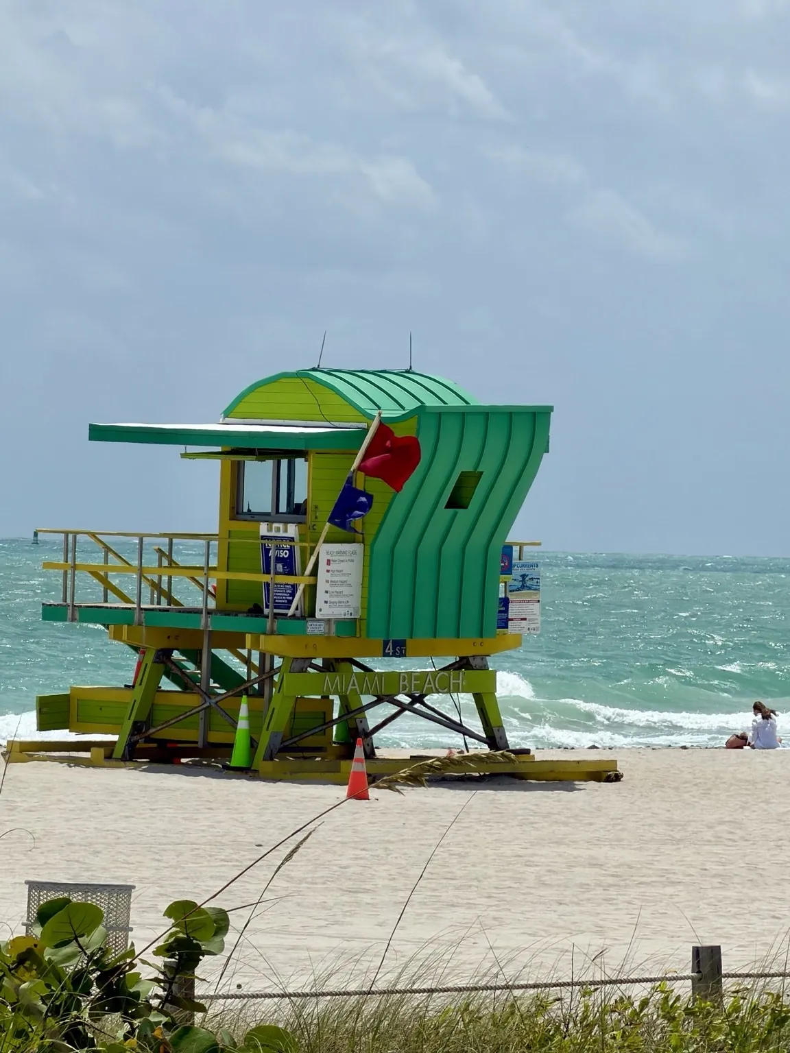A green and yellow lifeguard tower on the sand, with the turquoise sea behind it.