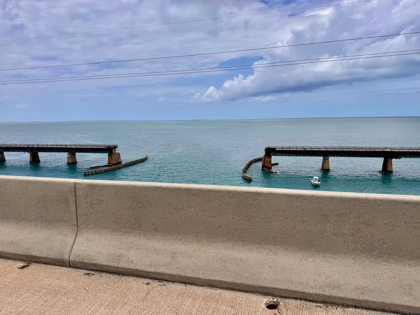 Two sections of the old bridge, broken in the middle, above the calm sea.