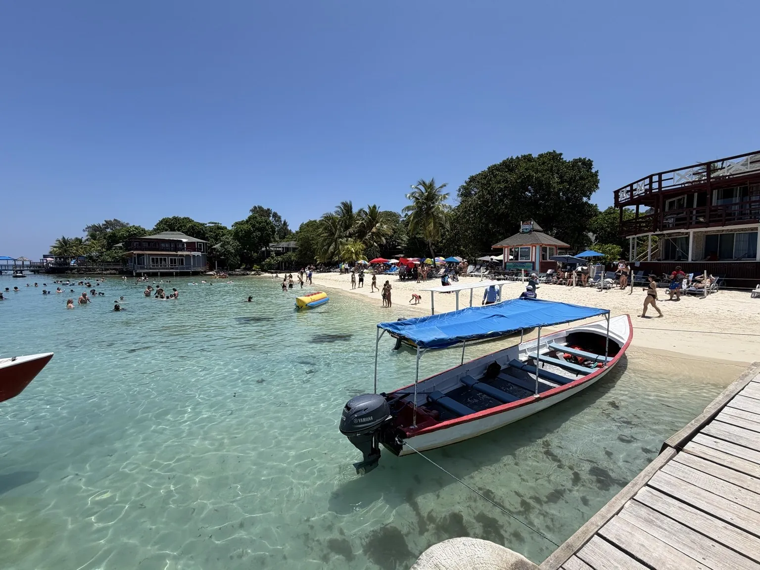 The clear turquoise water of the bay, with a blue-roofed boat and the beach behind it.