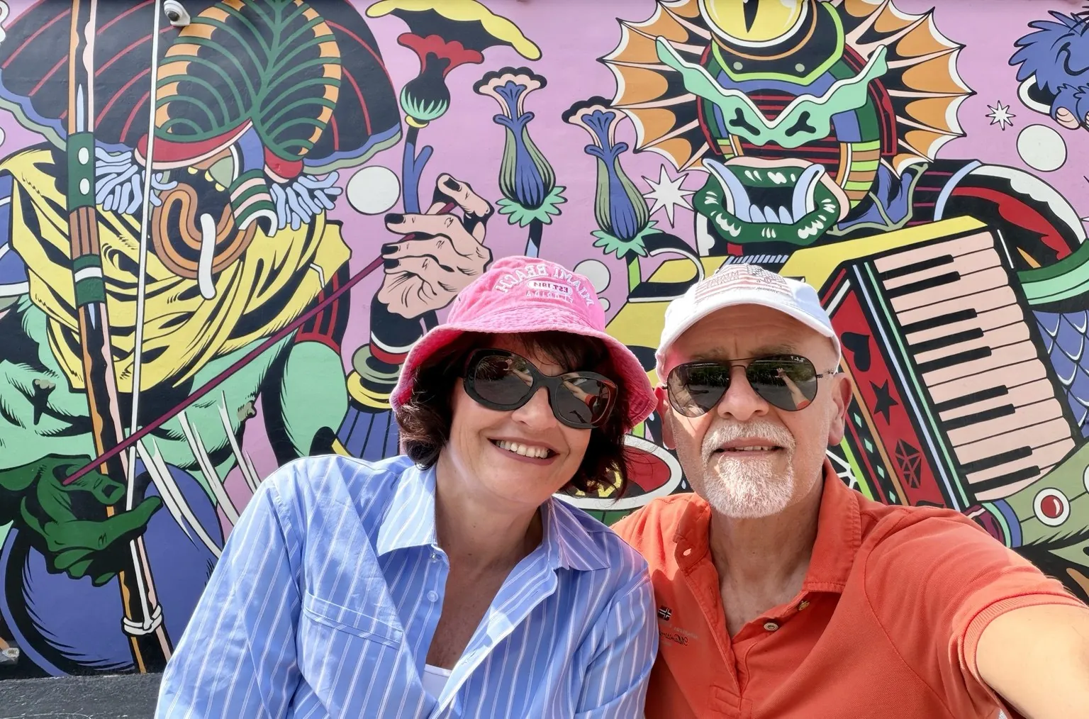 Anna and her companion, both in hats, in a selfie in front of a large, brightly coloured mural.