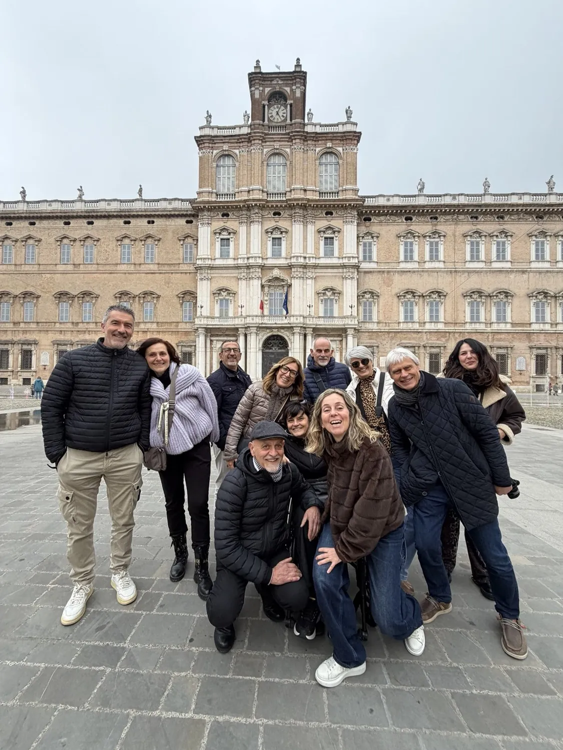 Il gruppo di amici sorridenti in Piazza Roma, con la lunga facciata del Palazzo Ducale alle spalle.